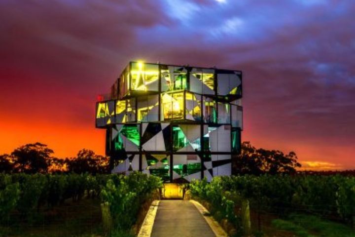 Geometric building with illuminated windows under dramatic sunset sky.