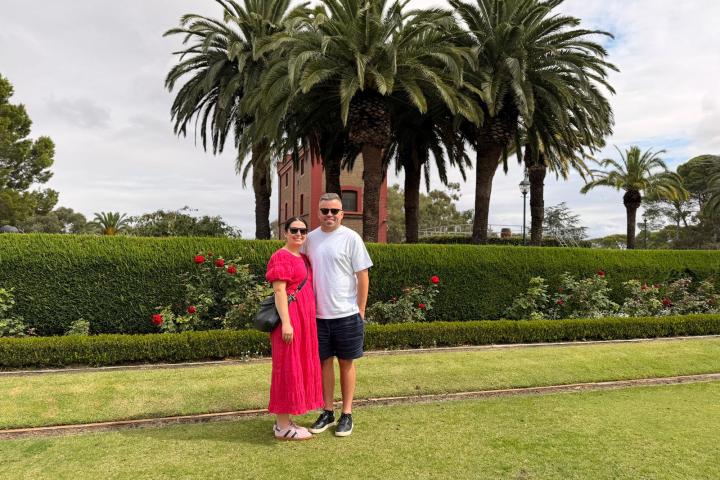 Couple posing in front of palm trees and hedges on a lawn.