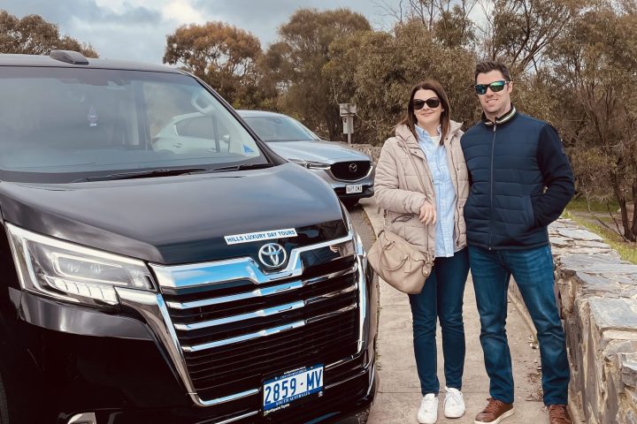 Two people standing next to a parked black van on a cloudy day.