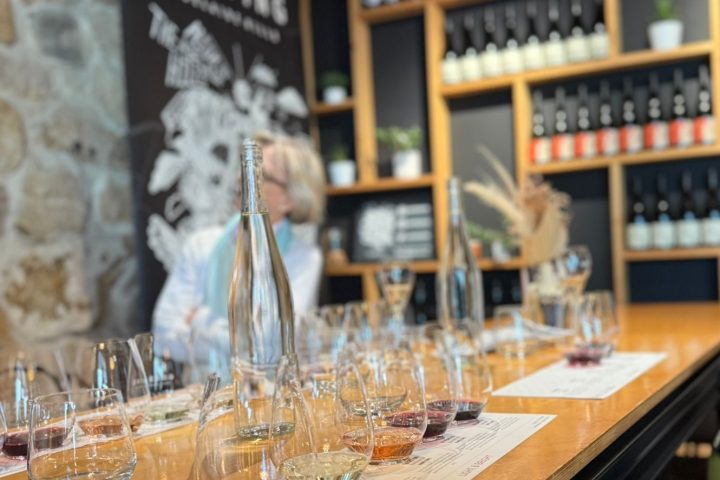 Two people at a wine tasting table with bottles and glasses in a rustic room.