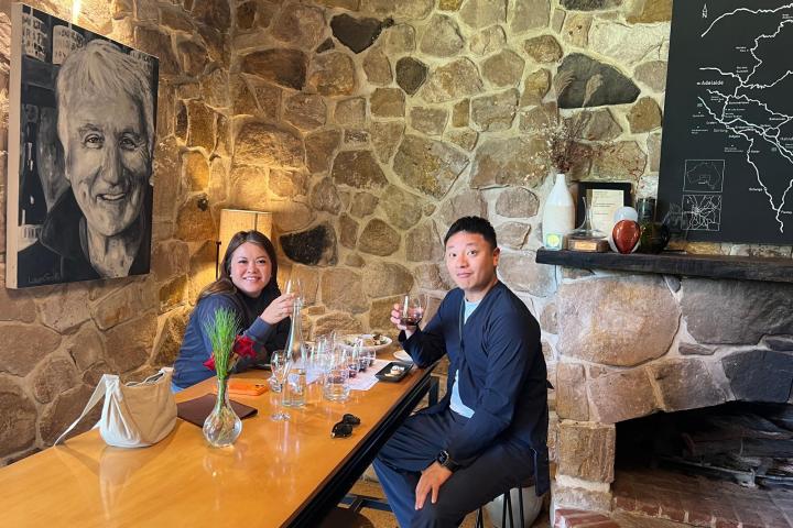 Two people sitting at a table with wine glasses in a stone-walled room.