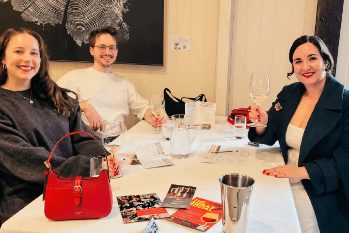 Three people sitting at a table with drinks and brochures, smiling.