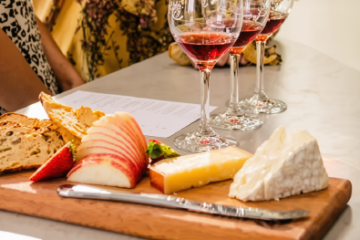 Cheese and fruit platter with three glasses of red wine on a table.