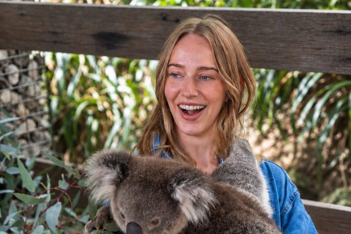 Woman holding a koala with greenery in the background.