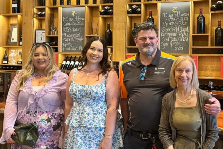Four people posing in front of wine shelves labeled with vine ages at a winery.