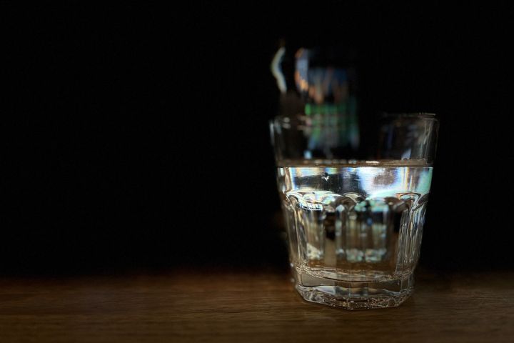 Half-filled glass of water on a wooden surface in low light.