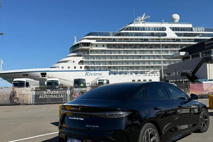 Black car parked near a large cruise ship under a clear blue sky.