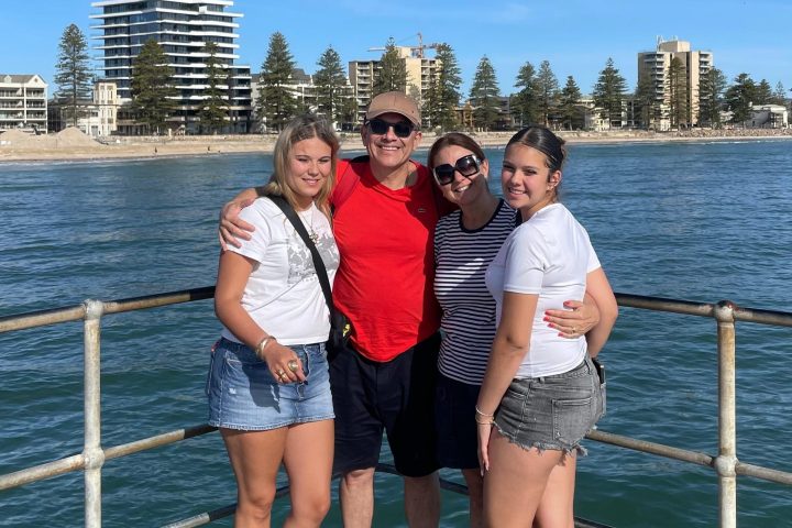 Four people standing on a pier with a cityscape and water in the background.