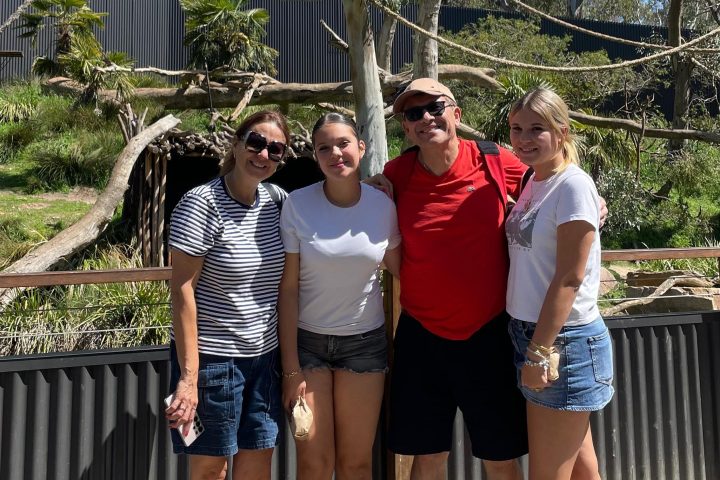 Group of four people posing in front of outdoor wildlife enclosure on a sunny day.