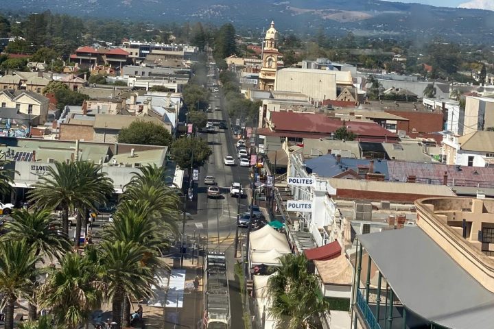 Aerial view of a town with palm trees, vehicles, and distant mountains under a clear blue sky.