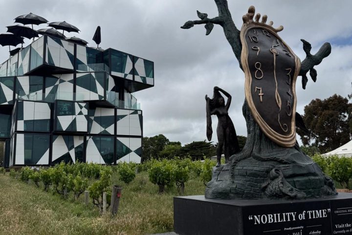 Modern geometric building and Salvador Dalí sculpture 'Nobility of Time' under cloudy sky.