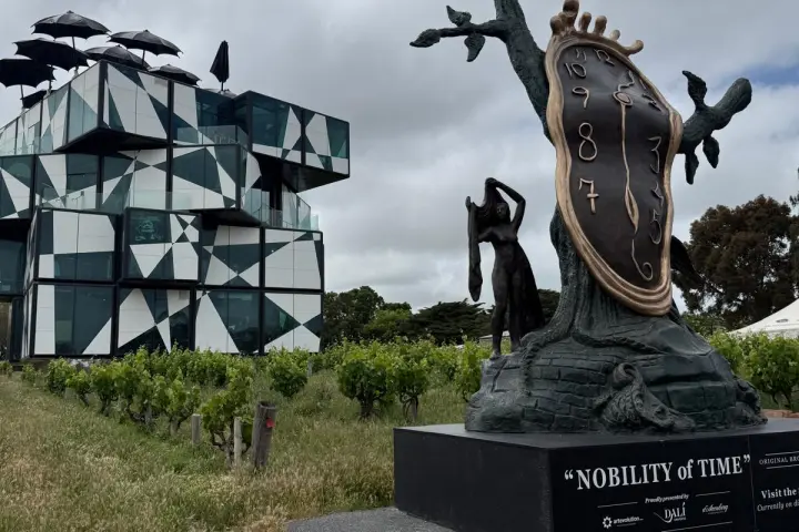 Modern geometric building and Salvador Dalí sculpture 'Nobility of Time' under cloudy sky.