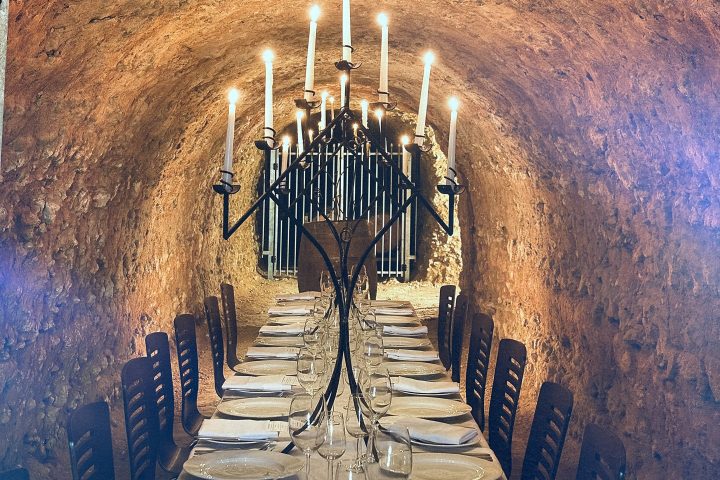 Long dining table in candle-lit stone cellar with empty plates and glasses.