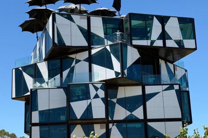 Modern building with geometric facade and black umbrellas on top, surrounded by greenery under a clear blue sky.
