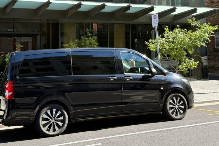 Black van parked on city street beside glass building.