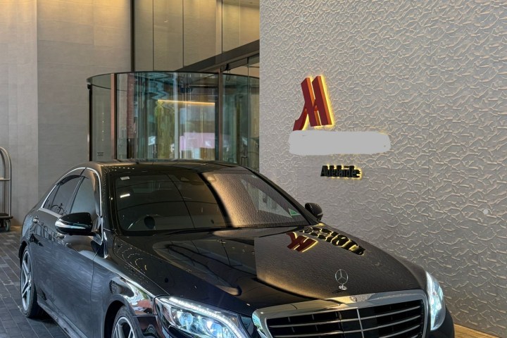 Black Mercedes parked by a hotel entrance with revolving doors.