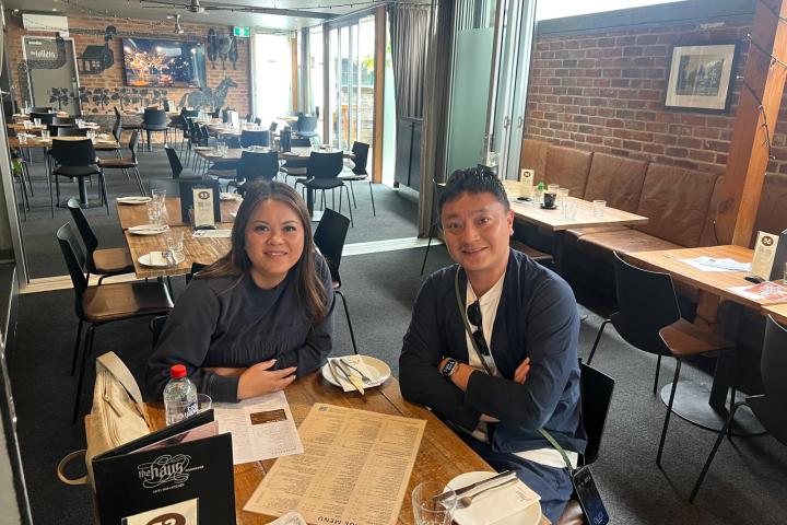 Two people sitting at a restaurant table with menus, smiling at the camera.